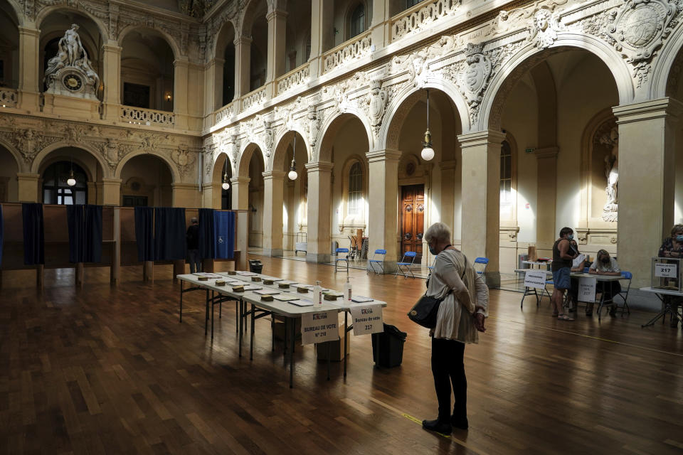 A voter picks up ballots before voting for the regional elections in Lyon, central France, Sunday, June 20, 2021. The elections for leadership councils of France's 13 regions, from Brittany to Burgundy to the French Riviera, are primarily about local issues like transportation, schools and infrastructure. But leading politicians are using them as a platform to test ideas and win followers ahead of the April presidential election. (AP Photo/Laurent Cipriani)