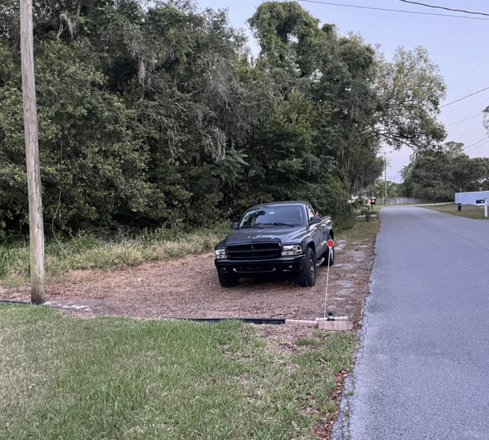 Car parked awkwardly on roadside with front wheels on the pavement and rear on grass