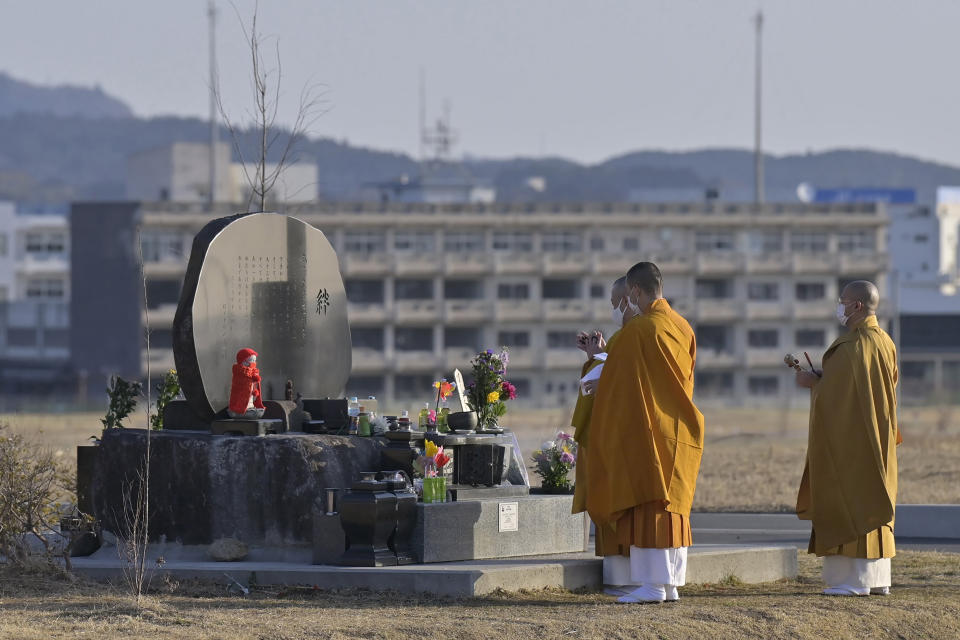 Buddhist monks offer a prayer for victims of the 2011 massive earthquake and tsunami, at a memorial cenotaph near former high school building, background, in Kesennuma, Miyagi prefecture, Japan Thursday, March 11, 2021. Thursday marks the 10th anniversary of the massive earthquake, tsunami and nuclear disaster that struck Japan's northeastern coast. (Yohei Nishimura/Kyodo News via AP)