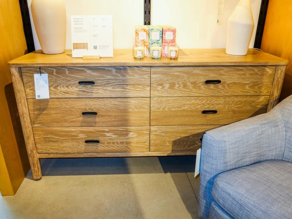 A wooden dresser with black handles and a gray chair in the foreground. White lamps and candles sit on the dresser.