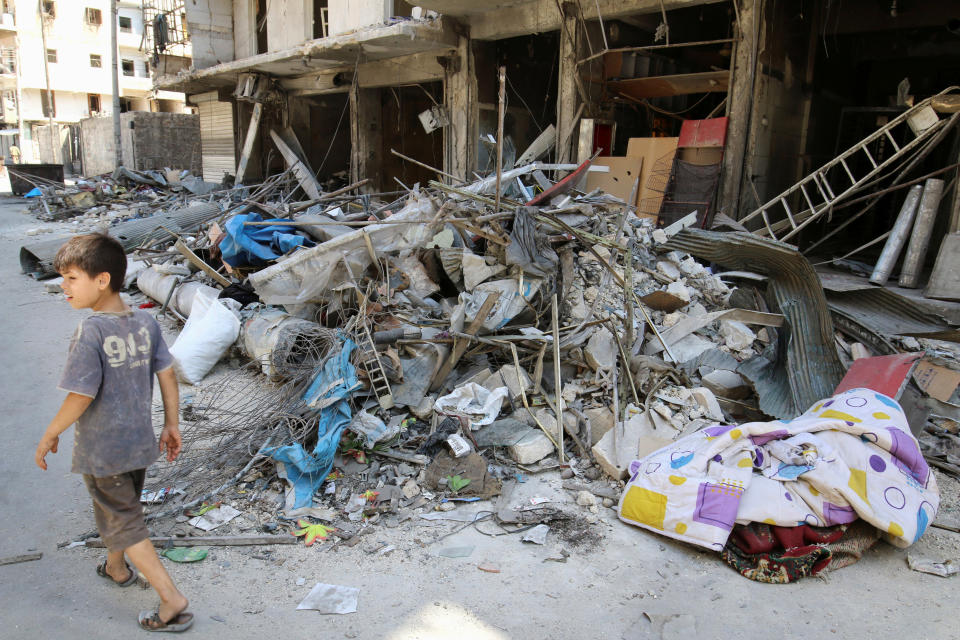 A boy walks past damaged shops in the rebel held Tariq al-Bab neighborhood of Aleppo, Syria on Aug. 22, 2016.