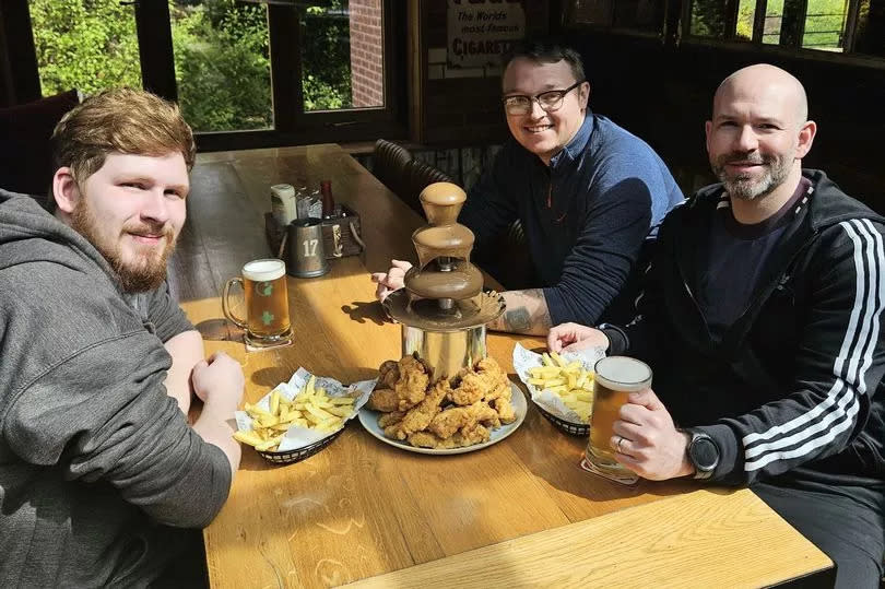 Three men around a fried chicken with a gravy fountain meal