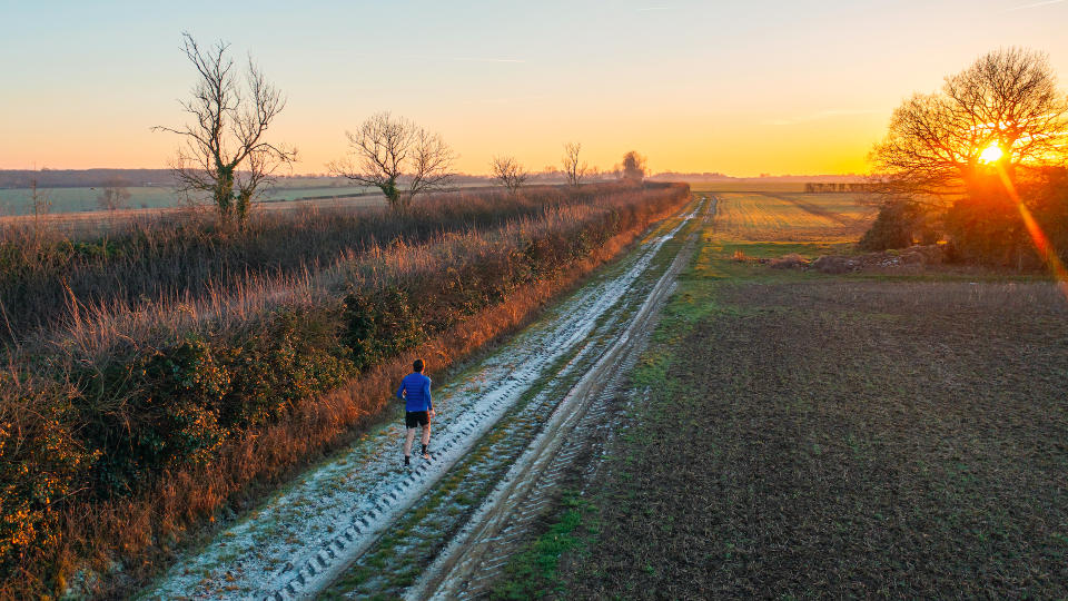 Elevated/drone view of a runner on a frosty trail from the UK countryside at sunset - 5 tips for night running