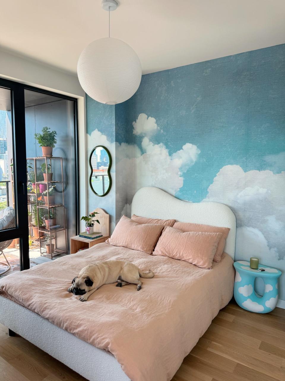 A bedroom with a wall covered in wallpaper that looks like a sky.