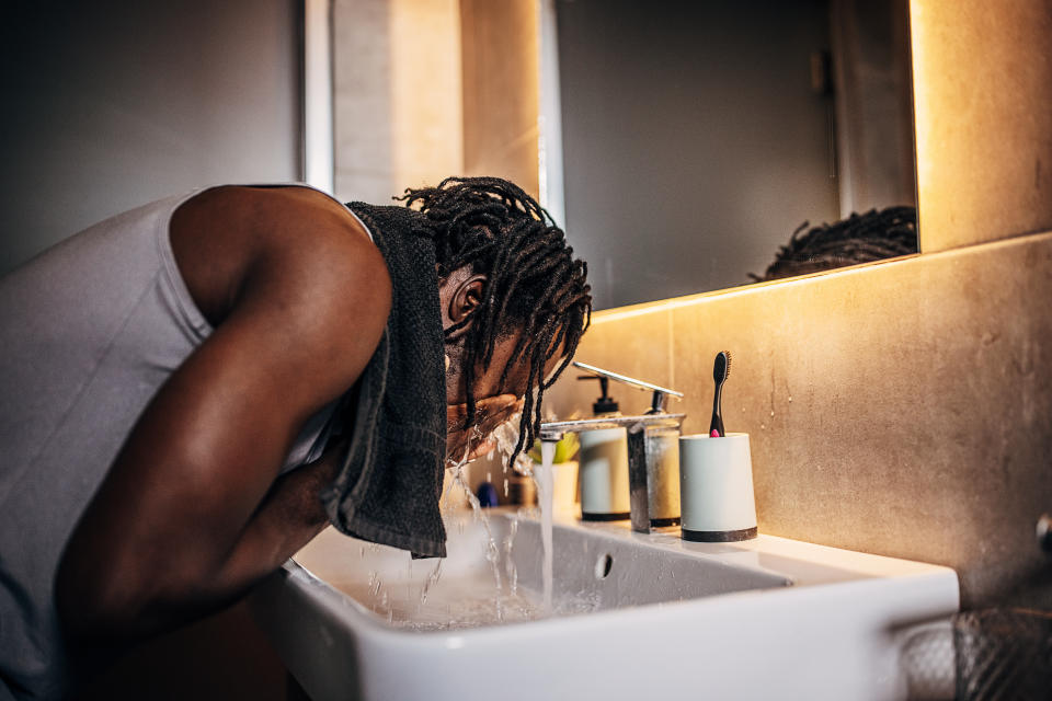 A man, a handsome black male, washes his face in the bathroom in the morning.