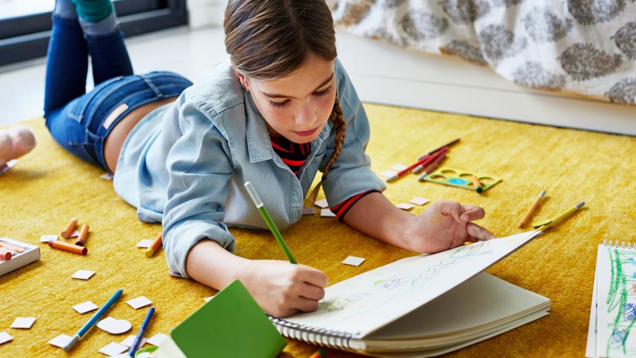 young girl on floor drawing with color pencils