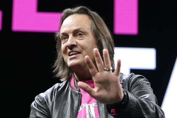 T-Mobile CEO John Legere smiling with his left hand up