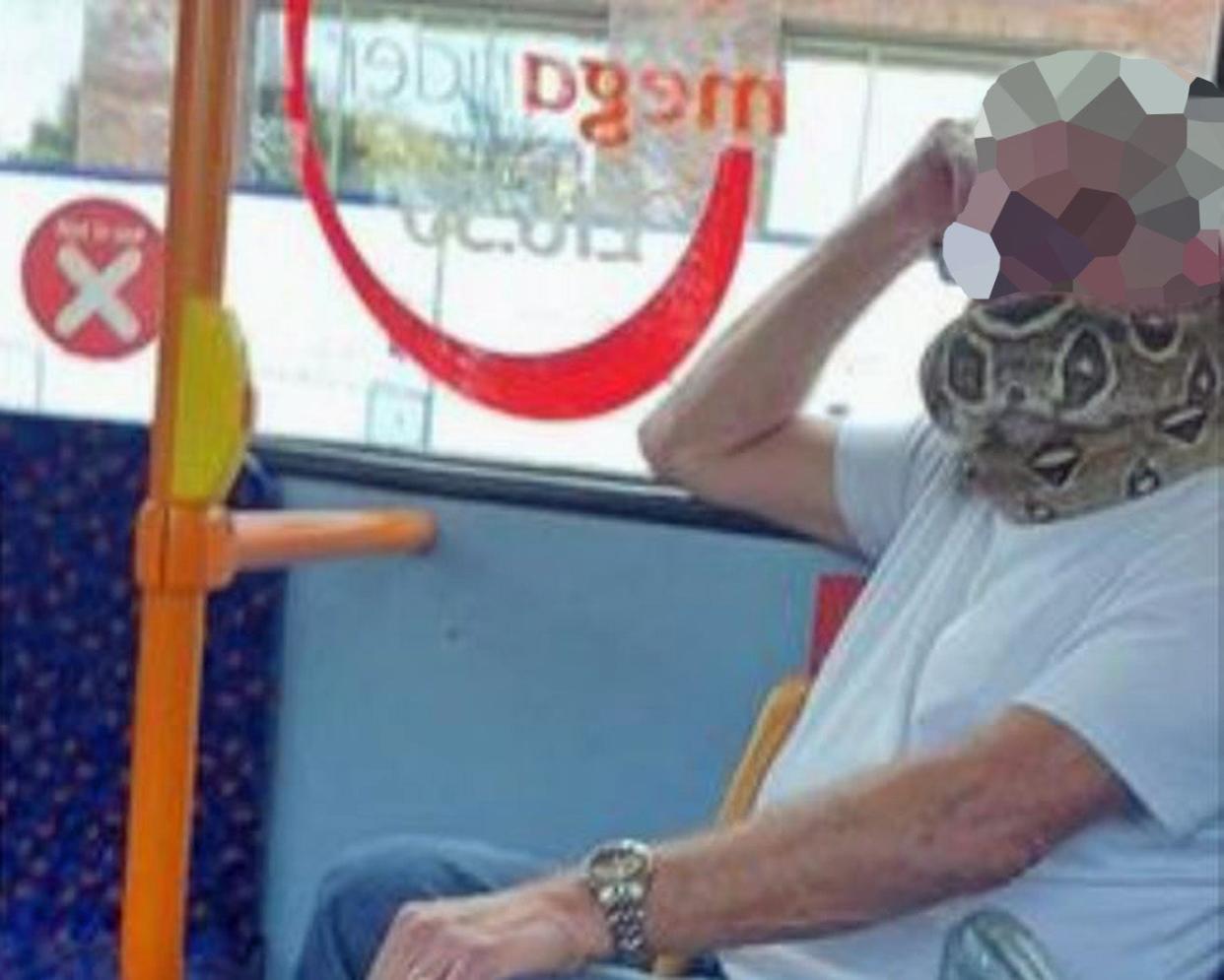 A man riding on a bus in Salford using a snake as a face mask (PA)