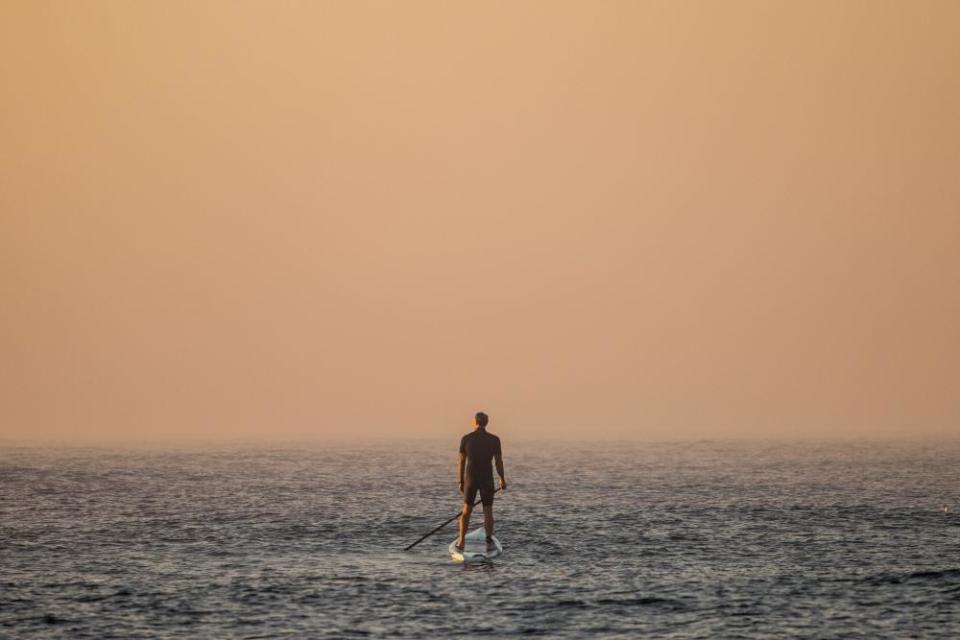 A man on a paddleboard looks out to a red, hazy sky