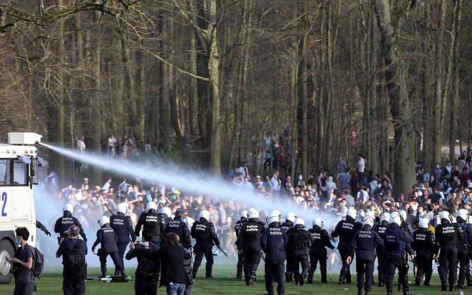 Bystanders and demonstrators are soaked by a Belgian police water canon as police officers surround them at the Bois de la Cambre parc, in Brussels, during a unauthorised rally, for a fake concert announced on social media as an April Fool's Day prank. - FRANCOIS WALSCHAERTS/AFP