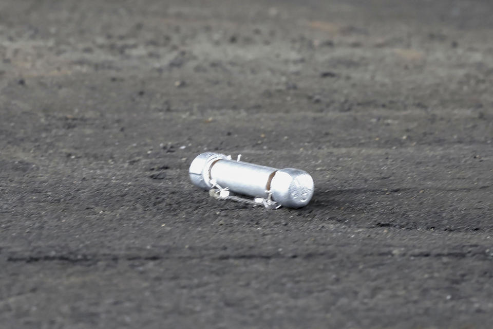 A suspicious object is seen on the ground where a suspect was arrested before Japanese Prime Minister Fumio Kishida was to begin his speech, at the Saikazaki port in Wakayama prefecture, western Japan, Saturday, April 15, 2023. Kishida was evacuated unharmed Saturday after someone threw an explosive device in his direction while he was campaigning at the fishing port in western Japan, officials said.(Kyodo News via AP)