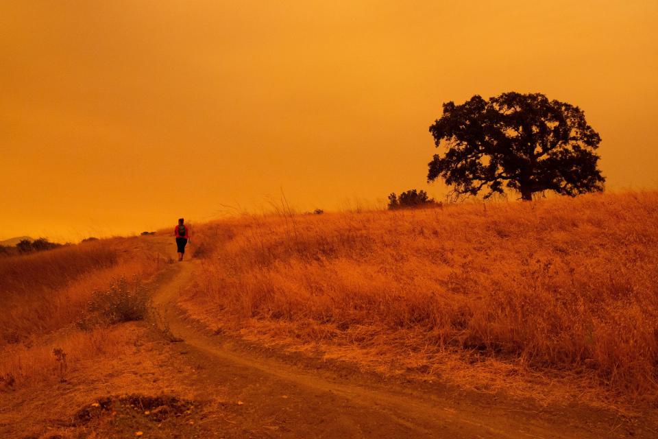 A hiker walks below an orange sky filled with wildfire smoke on the Limeridge Open Space hiking trails in Concord, California on September 9, 2020. / Credit: BRITTANY HOSEA-SMALL/AFP via Getty Images