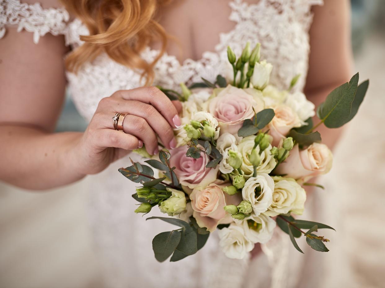 Bride holding a bouquet of pink, white, and green flowers with focus on lace detailing of wedding gown