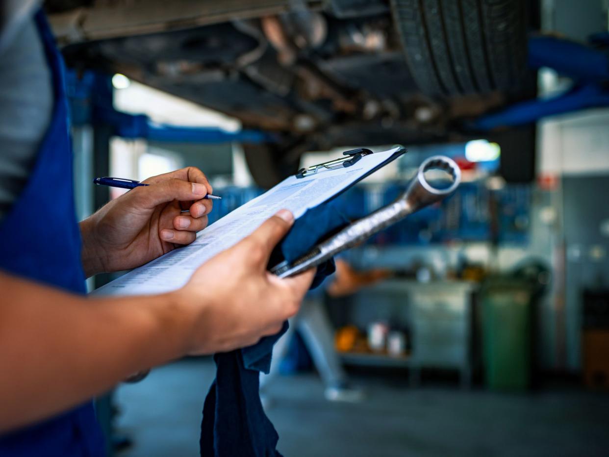 Unrecognizable Male mechanic under car preparing checklist in workshop. Photo of mechanic taking notes under a car.