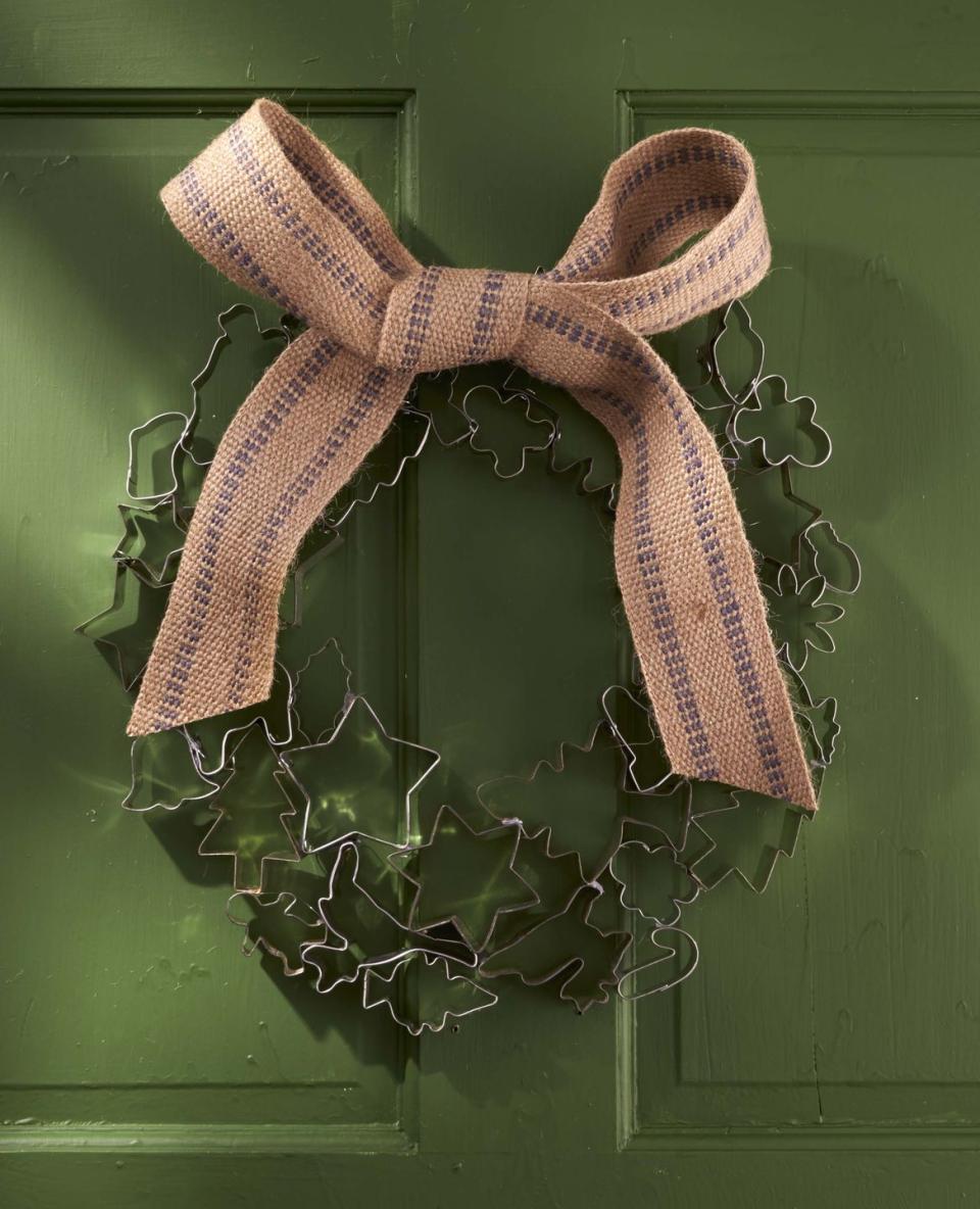 a wreath made from vintage cookie cutter hung on a dark green door adorned with a large jute bow