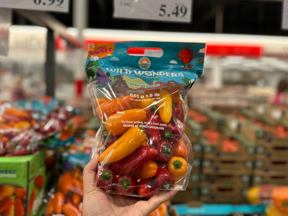 A hand holds a bag with a blue label full of small yellow, orange, and red peppers at Costco