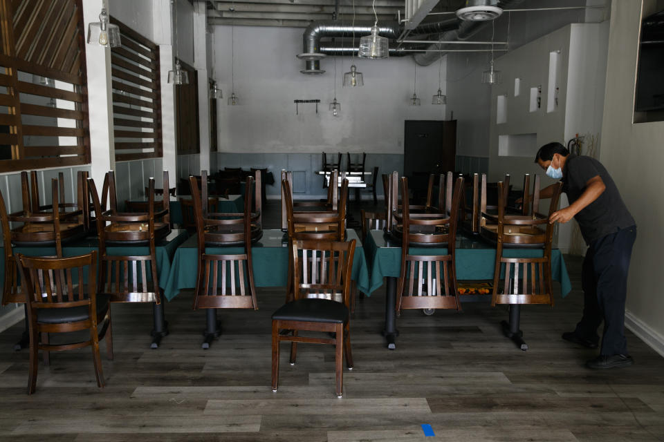 Fabian Nahui, the owner of a Peruvian restaurant, arranges chairs Monday, July 6, 2020, in Los Angeles. The coronavirus is blamed for over a half-million deaths worldwide, including more than 130,000 in the U.S., according to the tally kept by Johns Hopkins University. (AP Photo/Jae C. Hong)