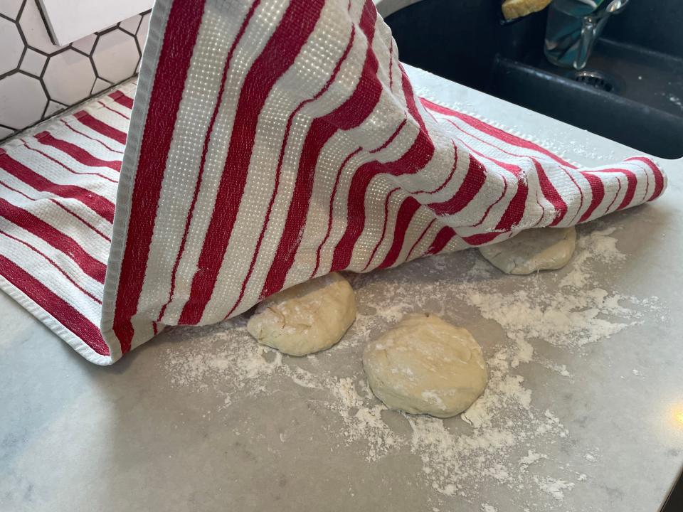 dough balls resting on a countertop under a striped kitchen towel