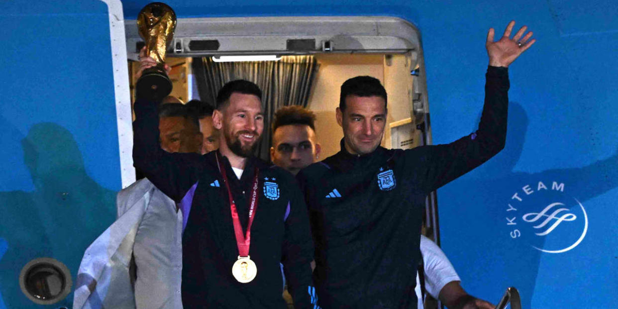 Argentina's captain and forward Lionel Messi (L) holds the FIFA World Cup Trophy alongside Argentina's coach Lionel Scaloni as they step off a plane upon arrival at Ezeiza International Airport after winning the Qatar 2022 World Cup tournament in Ezeiza, Buenos Aires province, Argentina on December 20, 2022. (Photo by Luis ROBAYO / AFP)