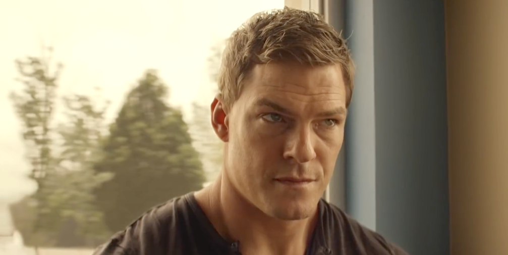 alan ritchson as jack reacher in amazon series reacher, sitting in a cafe wearing a black tshirt