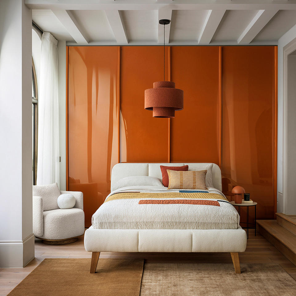 Neutral bedroom with white upholstered bed on a wooden floor against a caramel coloured feature wall