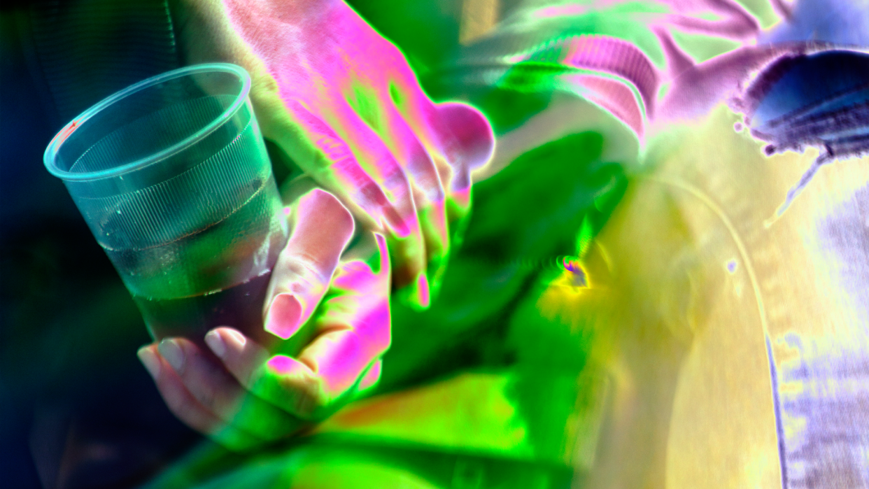 The effect of roofies, conveyed by the hands of a woman contoured in pink and green, holding a drink.