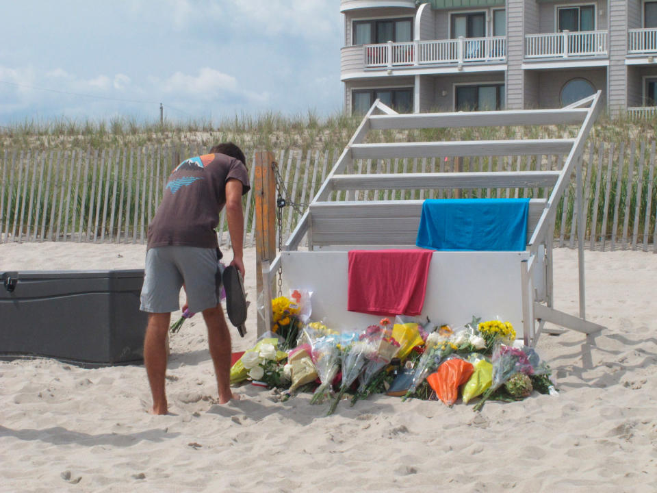 Michael Cordiano, a lifeguard in Berkeley Township, lays flowers on Tuesday at the base of a lifeguard stand.