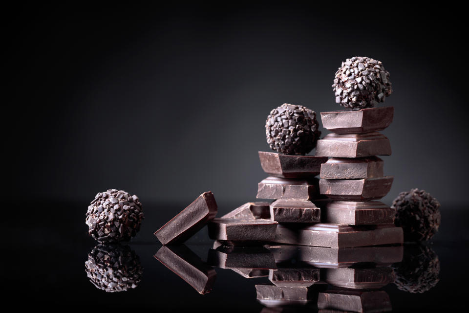 Chocolate candies with broken chocolate pieces on black reflective background. Copy space.