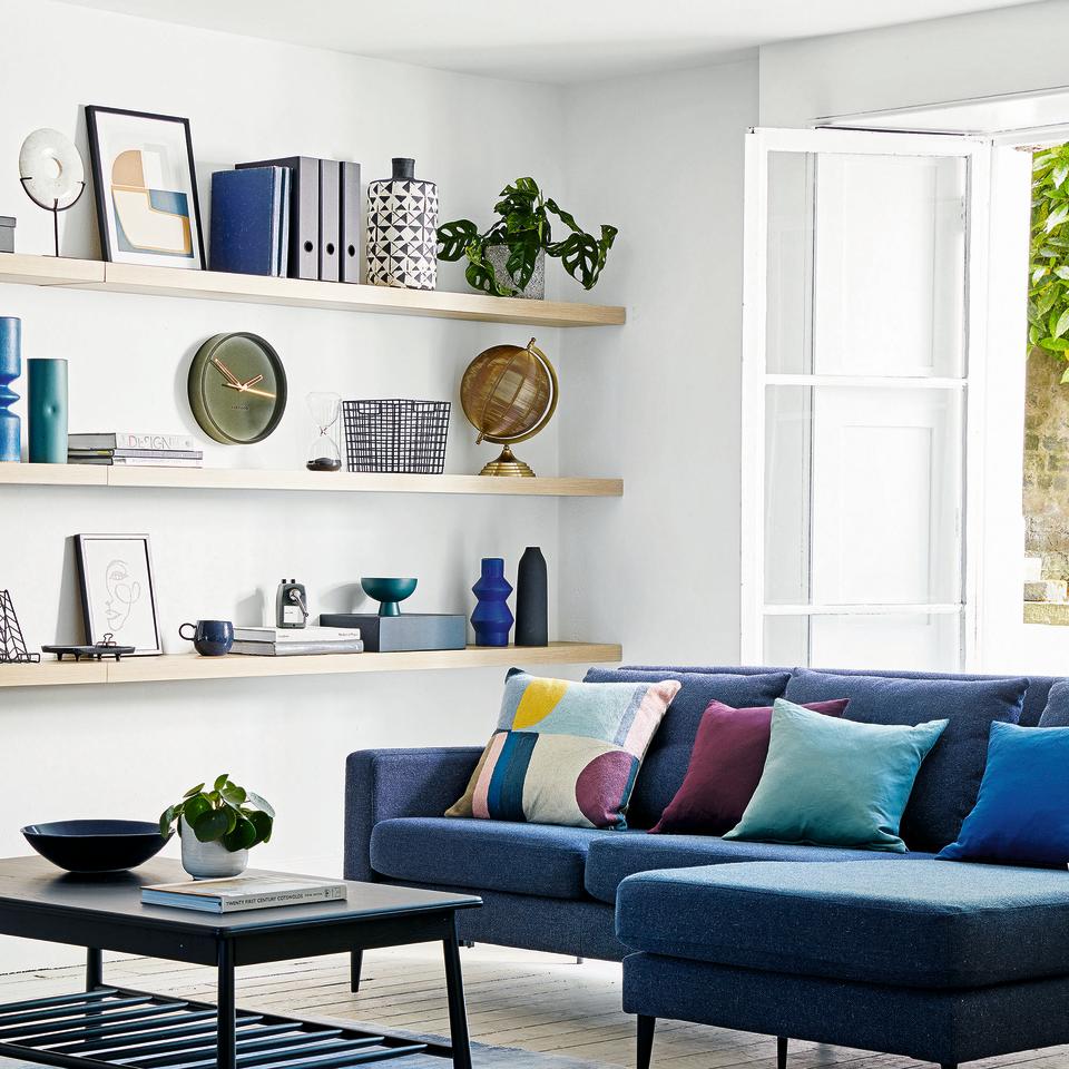 Living room with blue sofa and cushions and white shelves along wall.