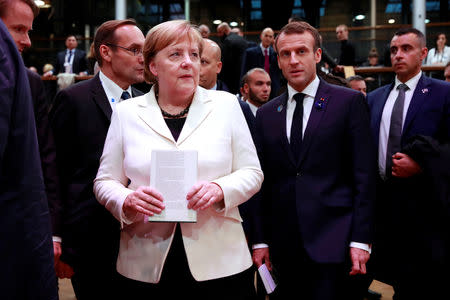 German Chancellor Angela Merkel and French President Emmanuel Macron hold books they will leave at the peace library at the Paris Peace Forum as part of the commemoration ceremony for Armistice Day, 100 years after the end of the First World War, in Paris, France, November 11, 2018. REUTERS/Gonzalo Fuentes/Pool