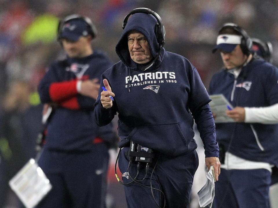 Bill Belichick gives a thumbs-up from the sideline as assistant coaches stand behind him.