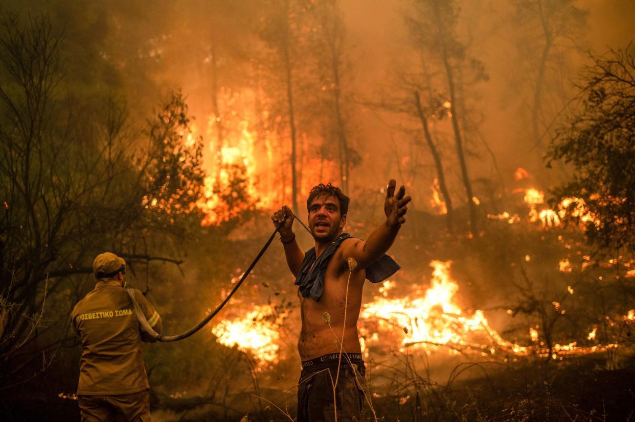 TOPSHOT - A local resident gestures as he holds n empty water hose during an attempt to extinguish forest fires approaching the village of Pefki on Evia (Euboea) island, Greece's second largest island, on August 8, 2021. - Hundreds of Greek firefighters fought desperately on August 8 to control wildfires on the island of Evia that have charred vast areas of pine forest, destroyed homes and forced tourists and locals to flee. Greece and Turkey have been battling devastating fires for nearly two weeks as the region suffered its worst heatwave in decades, which experts have linked to climate change. (Photo by ANGELOS TZORTZINIS / AFP) (Photo by ANGELOS TZORTZINIS/AFP via Getty Images)