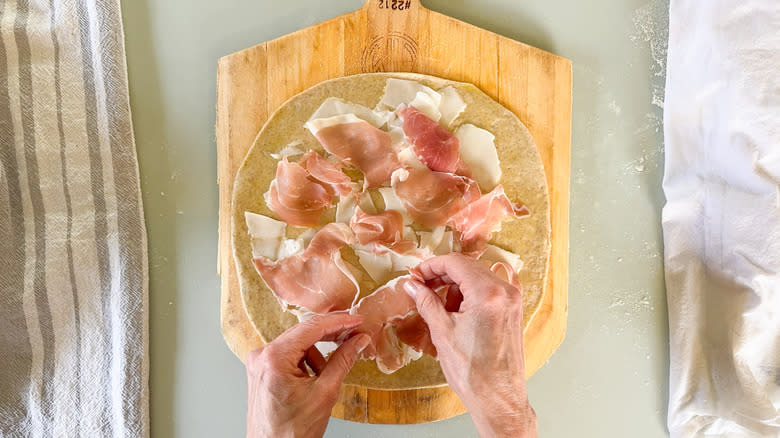 Placing prosciutto on flatbread with shaved goat gouda on pizza peel