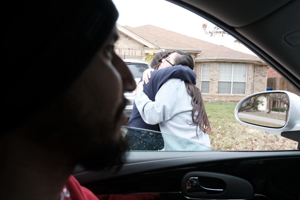Two people hug, as seen from the inside of a car.