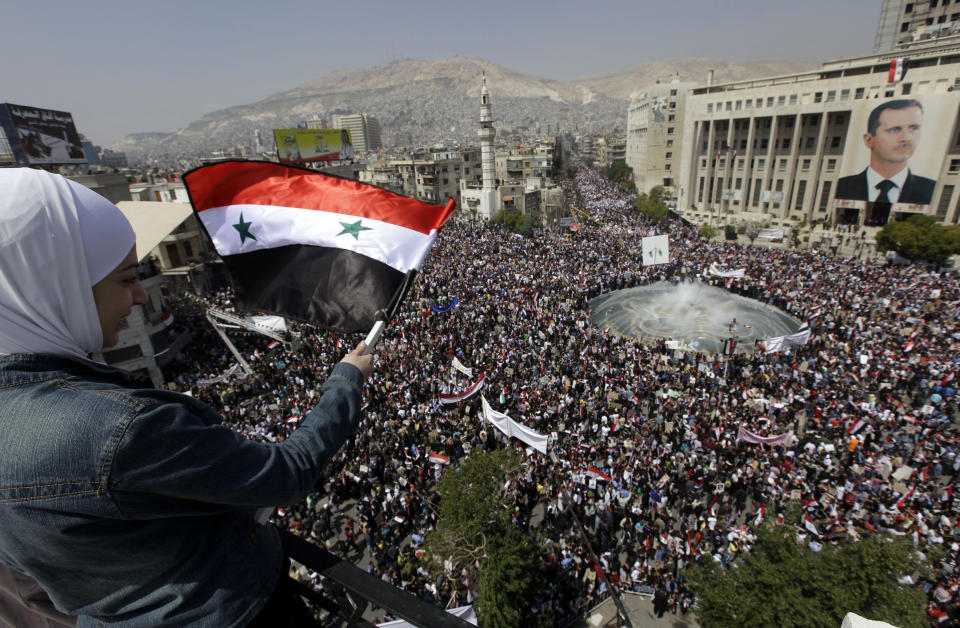 FILE - A supporter of Syrian President Bashar Assad waves a Syrian flag as she looks over a crowd gathered to show support for their president in Damascus, Syria, Tuesday, March 29, 2011. Ten years ago, an uprising in Tunisia opened the way for a wave of popular revolts against authoritarian rulers across the Middle East known as the Arab Spring. For a brief window as leaders fell, it seemed the move toward greater democracy was irreversible. Instead, the region saw its most destructive decade of the modern era. Syria, Yemen, Libya and Iraq have been torn apart by wars, displacement and humanitarian crisis. (AP Photo/Bassem Tellawi, File)