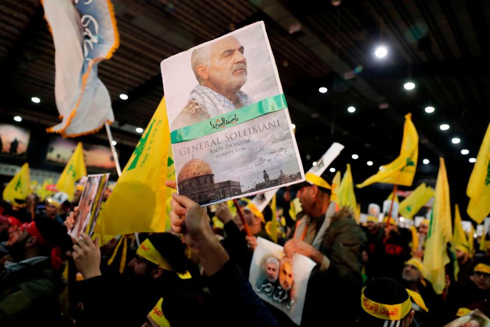 A supporter of Shiite Hezbollah movement holds a poster of slain Iranian Major General Qasem Soleimani as the movement's leader delivers a speech on a screen in the Lebanese capital Beirut's southern suburbs on January 5, 2020.