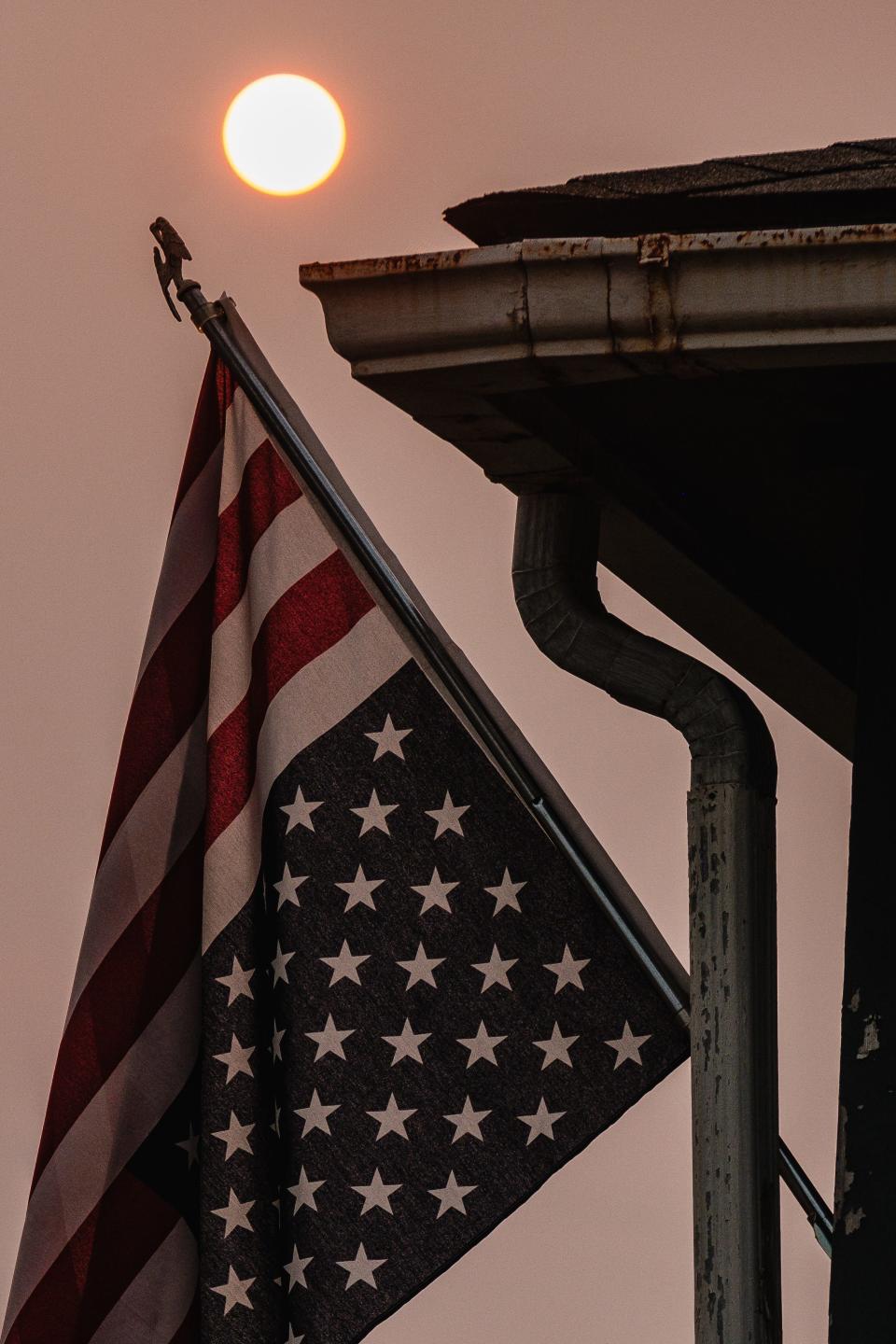 Sunrise is partially obscured by Canadian wildfire smoke in New Philadelphia as seen behind an upside down American flag, Tuesday, Aug. 1. According to the U.S. Flag Code, flying the American flag upside down is only meant to be done as a signal of dire distress in instances of extreme danger to life or property. The gesture has taken on more of political statement in recent times.