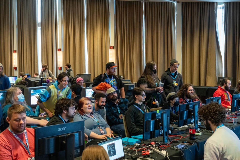 A conference room full of gamers and speed runners playing and watching games on various computer monitors.