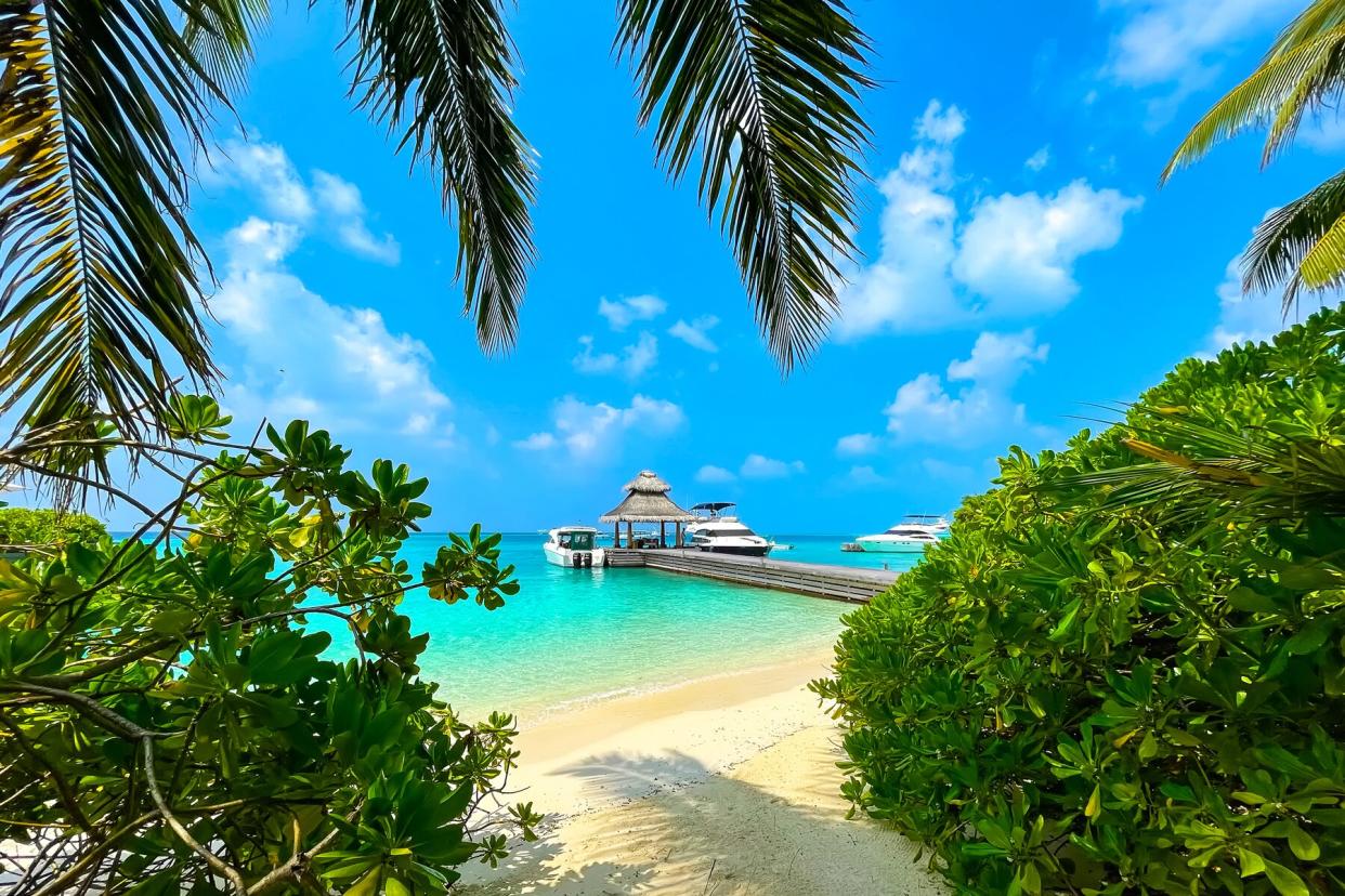 Panoramic landscape of Maldives beach and pier with speed boats and yachts on the horizon