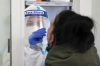 Lavinia Israel, a testing center employee, takes a sample from a customer for a quick test at a Corona testing center at the Kaufpark Nickern shopping center in Dresden, Germany, Friday, Dec. 3, 2021. (Sebastian Kahnert/dpa via AP)