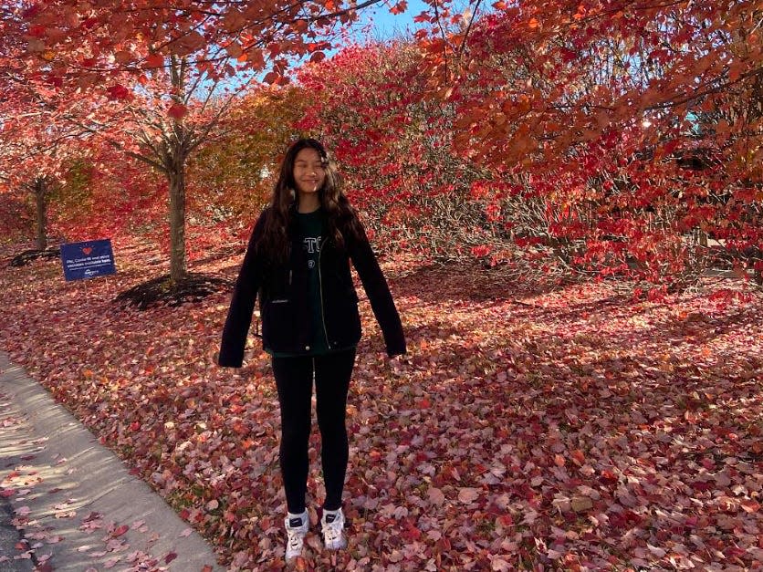 Valerie Do standing on the sidewalk surrounded by fallen leaves.