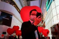 A man wearing a face mask takes a selfie in front of hearts celebrating Valentine's Day in front of shopping mall in Bangkok