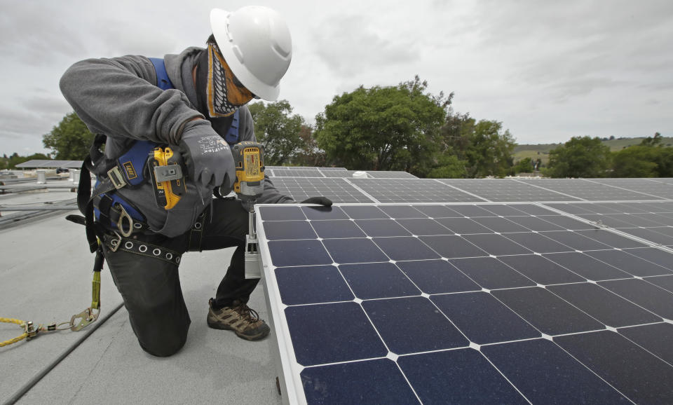 Gen Nashimoto, of Luminalt, installs solar panels in Hayward, Calif., on Wednesday, April 29, 2020. From New York to California, the U.S renewable energy industry is reeling from the new coronavirus pandemic, which has delayed construction and sowed doubts about major projects on the drawing board. (AP Photo/Ben Margot)