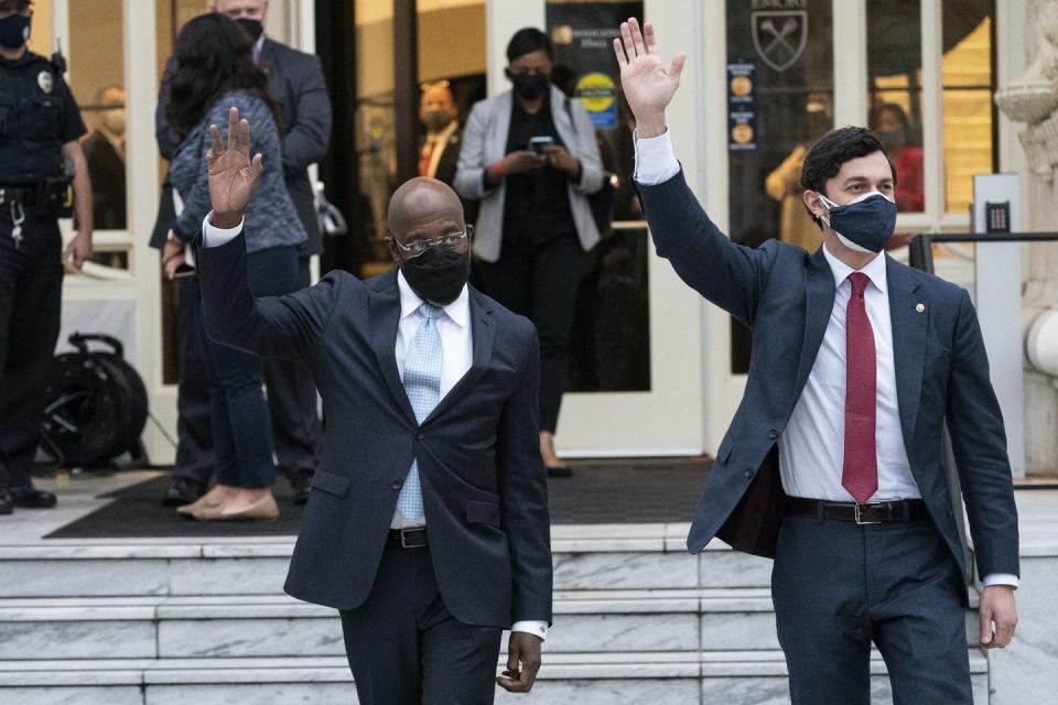 Two men in suits wave to a crowd