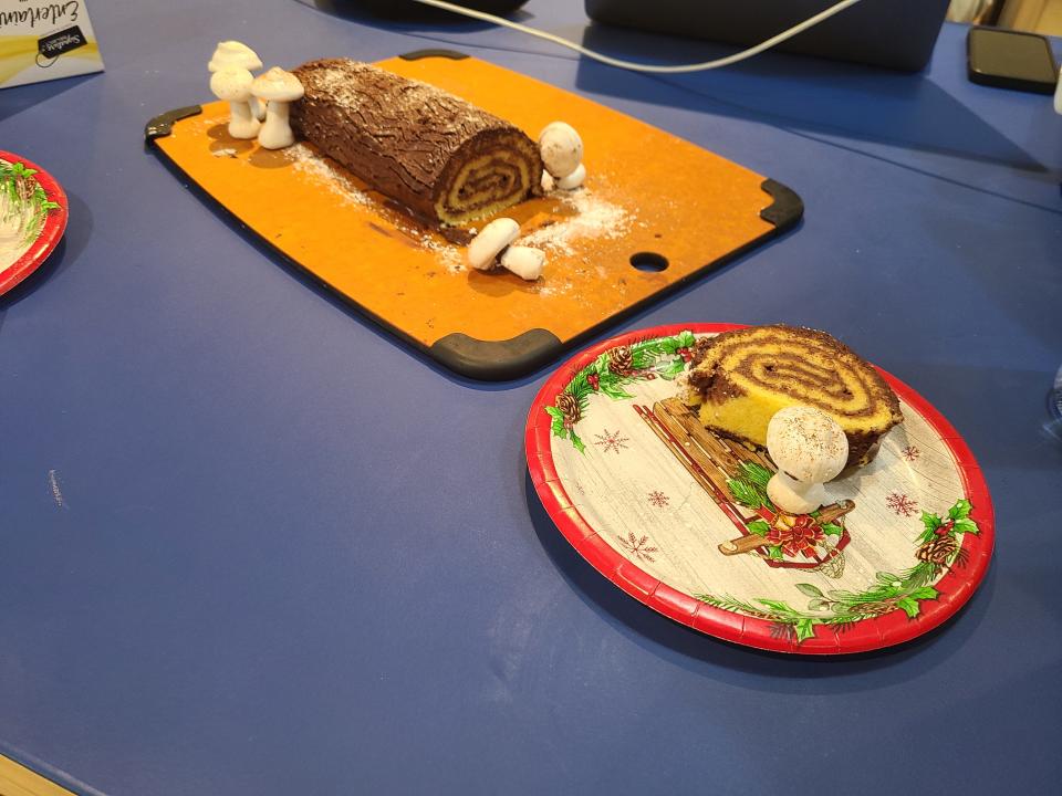 A yule log decorated with meringue mushrooms with a slice cut out of it.