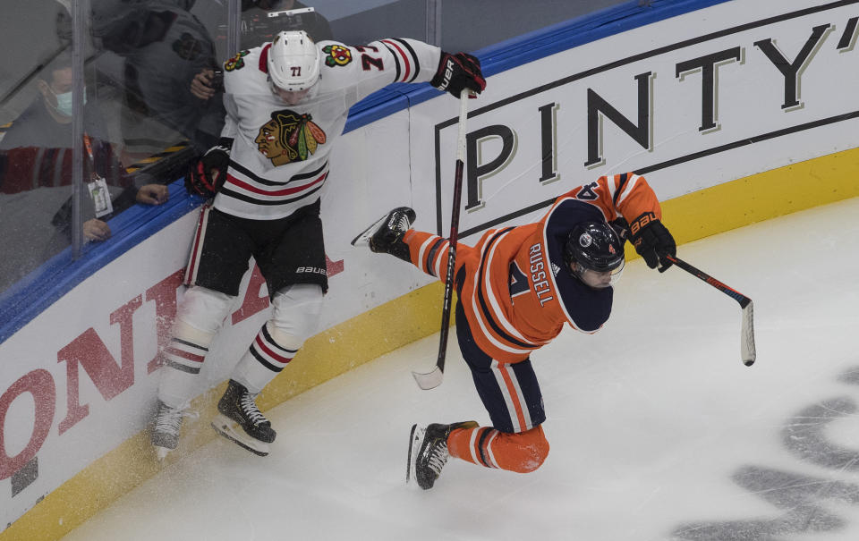 Edmonton Oilers' Kris Russell (4) is checked by Chicago Blackhawks' Kirby Dach (77) during the second period of an NHL Stanley Cup playoff hockey game in Edmonton, Alberta, Saturday, Aug. 1, 2020. (Jason Franson/The Canadian Press via AP)