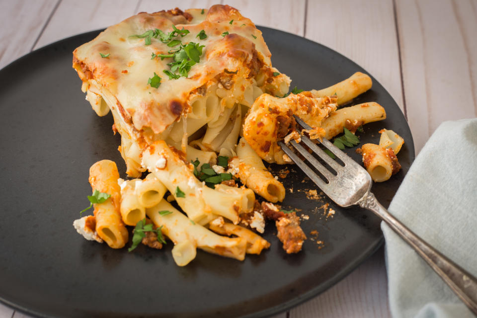 Plate with lasagna and pasta with garnish next to fork on a table