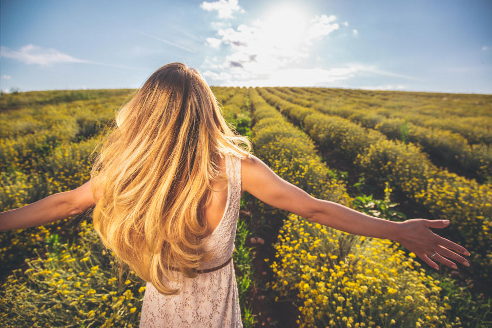 Photo of a young woman with arms outstretched walking down the immortelle flower field, enjoying life
