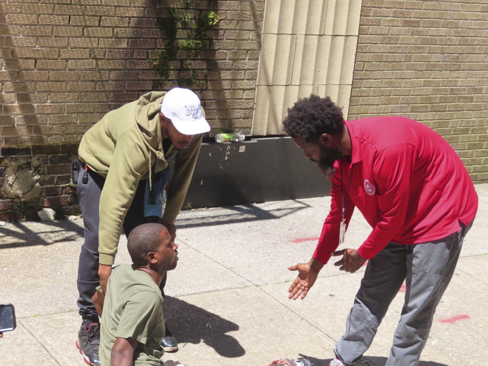 A city outreach worker reaches out to a man sprawled on a sidewalk in Atlantic City, N.J., on Monday, July 1, 2024, the date city officials announced implementation of programs to address homelessness. (AP Photo/Wayne Parry)