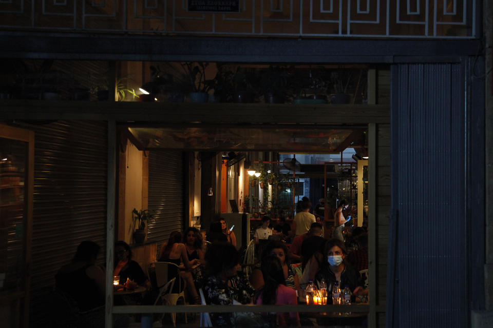 A woman wearing a mask sits with friends at a coffee shop at Ledra street a main shopping street in Nicosia, Cyprus, Tuesday, May 26, 2020. Cyprus took a major step toward a return to normality on Thursday when most restrictions of a two month-long stay-at-home order were lifted, allowing primary school kids to return to classes and hair salons and outdoor cafeterias to re-open. (AP Photo/Petros Karadjias)